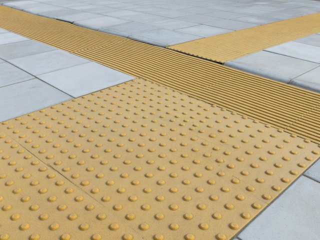 Close-up of raised tactile blister paving at a dropped kerb beside smooth paving slabs